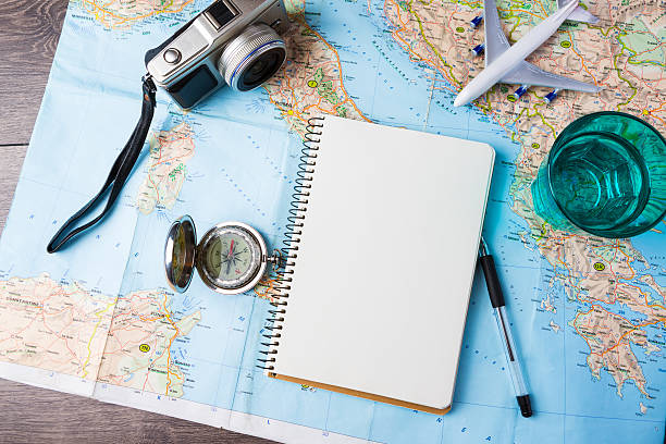 Travelling tools travel tourism agency table mockup tools compass, glass of water note pad, pen and toy airplane and touristic map on wooden table. Empty space you can place your text or information. explorer photos stock pictures, royalty-free photos & images