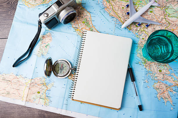 Travelling tools travel tourism agency table mockup tools compass, glass of water note pad, pen and toy airplane and touristic map on wooden table. Empty space you can place your text or information. travel stock pictures, royalty-free photos & images