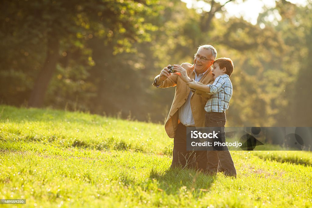 Grandparenting Grandfather and grandson having fun in park, they are photographing nature. 2015 Stock Photo