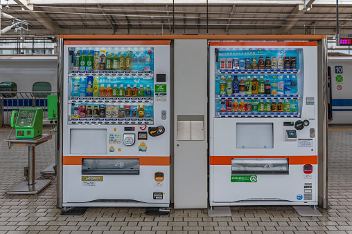 Kyoto, Japan - August 12, 2015: Soft drink vending machines and coin operated public phones on a station platform with a Shinkansen bullet train in the background