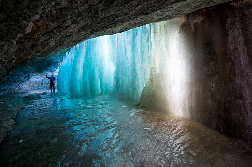 Woman takes a selfie in a grotto behind colorful turquoise tinted ice in a frozen waterfall in winter, Minnehaha Falls, Minneapolis, MN, USA