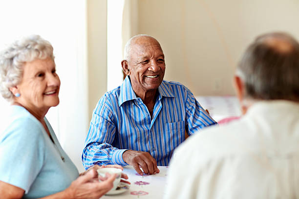 Senior man having coffee with friends Happy senior man having coffee with friends at table in nursing home nursing home stock pictures, royalty-free photos & images