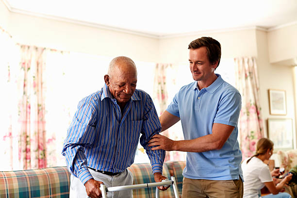 caretaker assisting senior man with walker - group of people aging process home interior indoors stock-fotos und bilder