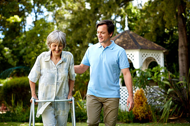 caretaker assisting senior woman in using walker - caretaker стоковые фото и изображения