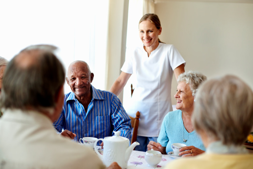 Happy female caretaker with senior people having coffee at table in nursing home