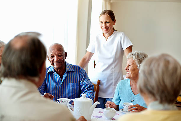 Caretaker with senior people enjoying coffee break Happy female caretaker with senior people having coffee at table in nursing home retirement community stock pictures, royalty-free photos & images