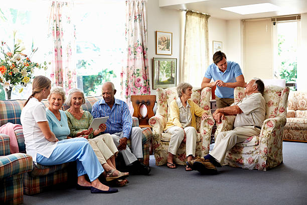 Caretaker with retired people in nursing home Male caretaker spending leisure time with retired people in nursing home retirement community stock pictures, royalty-free photos & images