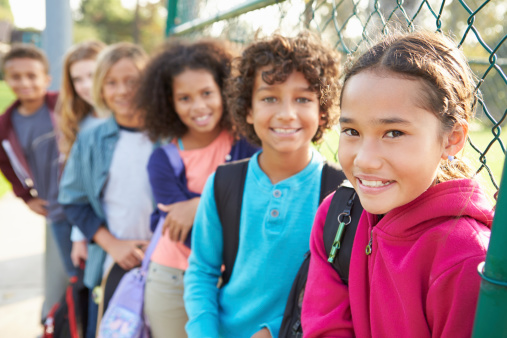 Group Of Young Children Hanging Out In Playground Smiling To Camera