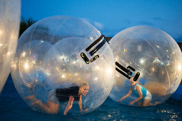 Two girls roll inside giant plastic balls Two girls roll around inside giant plastic balls floating in water on a summer evening at the county fair, Rochester, MN, USA zorbing stock pictures, royalty-free photos & images