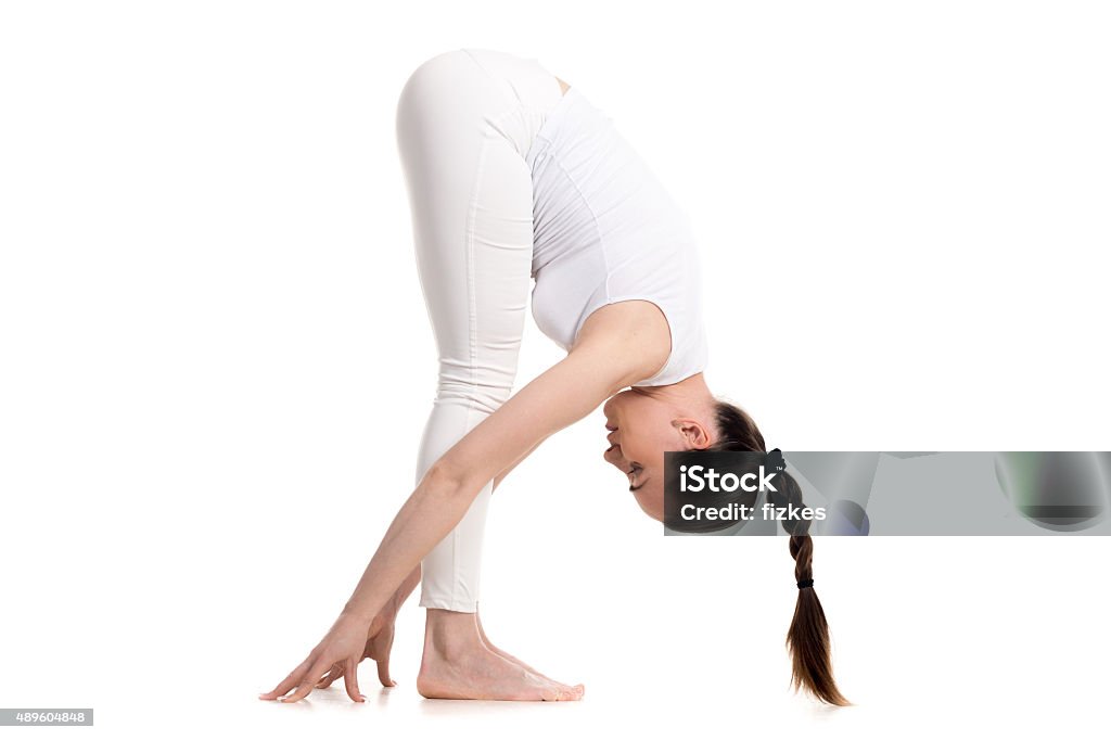 Yogi female standing in Intense Stretch Pose Sporty beautiful young woman in white sportswear with cute braid hairstyle doing Standing Forward Bend, Uttanasana pose, profile studio full length view, isolated, part of Surya Namaskar series 2015 Stock Photo