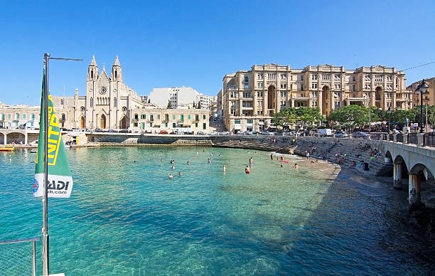 St Julians church St Julians, Malta - September 13, 2015: Our Lady of Mount Carmel Church stands tall with bathers on the small beach in Balluta Bay in St Julian's, Malta on a sunny day in September. st julians bay stock pictures, royalty-free photos & images