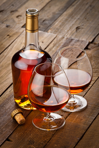 Two cognac snifters beside an open cognac bottle shot on rustic wood table. Low key DSRL studio photo taken with Canon EOS 5D Mk II and Canon EF 70-200mm f/2.8L IS II USM Telephoto Zoom Lens