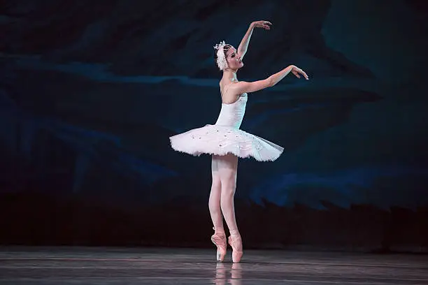 Prima ballerina white swan on the stage gracefully dancing on decorative theatrical background.