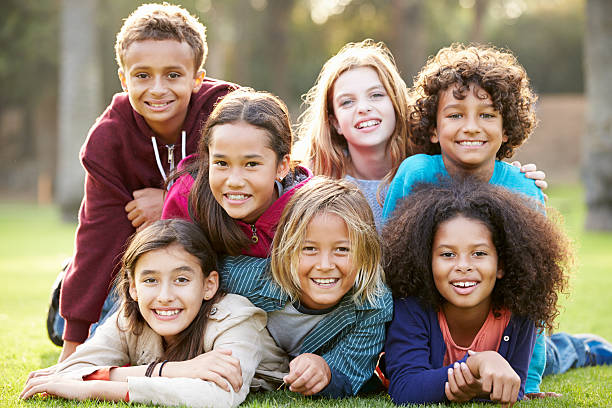 Group Of Children Lying On Grass Together In Park Group Of Children Lying On Grass Together In Park Smiling To Camera primary age child stock pictures, royalty-free photos & images