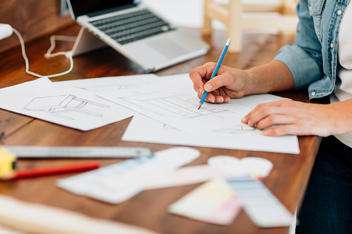 Unrecognizable Female carpenter or furniture designer sketching new furniture and preparing new project. Selective focus to hand and pencil. Shallow DOF. Shot with Canon EOS 5Ds with 85/1.2L 50 Mpx.