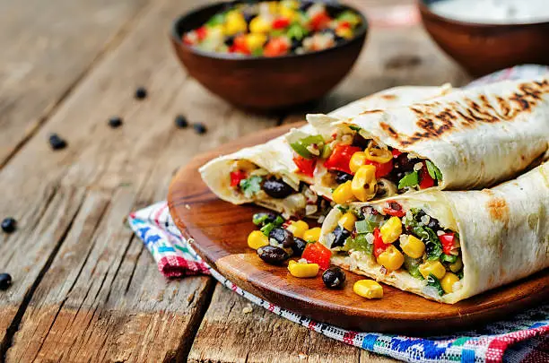 pepper corn black bean quinoa burritos on a dark wood background. the toning. selective focus