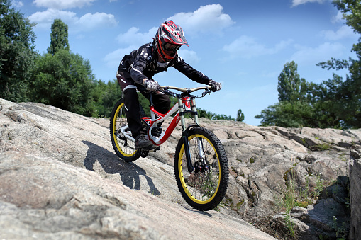 Sportsman in sportswear on a mountain bike rides on the stones in extreme style downhill
