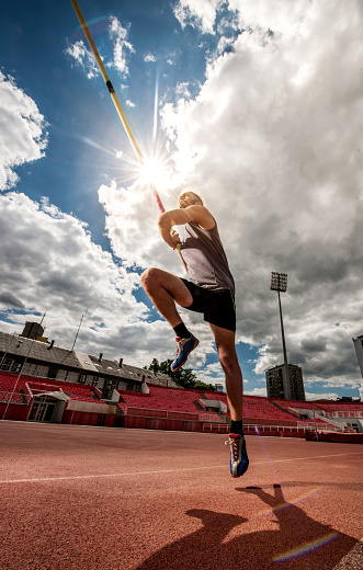 Low angle view of young athletic man in a jump with pole vault on a stadium.