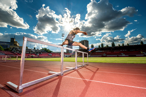 Young athletic man making an effort while jumping hurdles on a stadium.