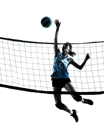Low angle view of young woman volleyball player jumping to spiking volleyball at night.