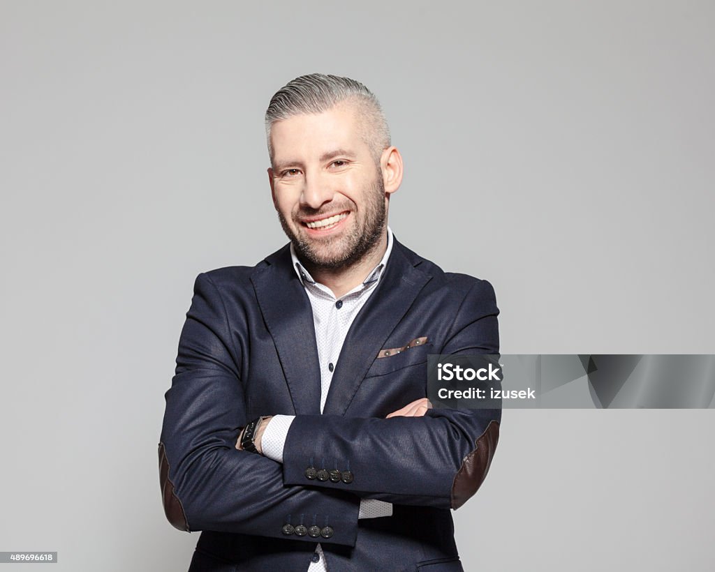 Successful bearded grey hair businessman Portrait of elegant bearded grey hair businessman standing against grey background with arms crossed and smiling at camera. Studio shot, one person.  2015 Stock Photo