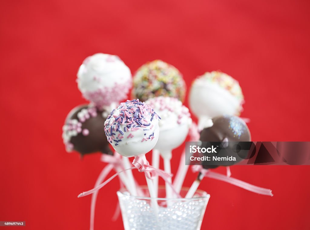 Brownie Cakepops over Red Background Delicious brownie cakepops over red background. The cakepops are covered with white and dark chocolate and sprinkled with sweet rounded shavings. The cakepop are standing in a glass. Cake Stock Photo