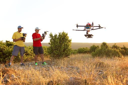Two men standing on rural landscape using remote control to fly drone.