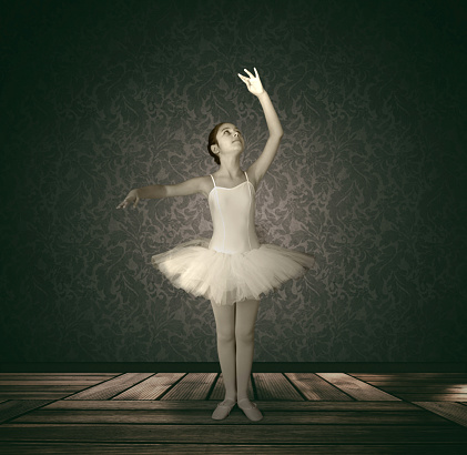 Young ballet dancer in dark room with wooden floor.