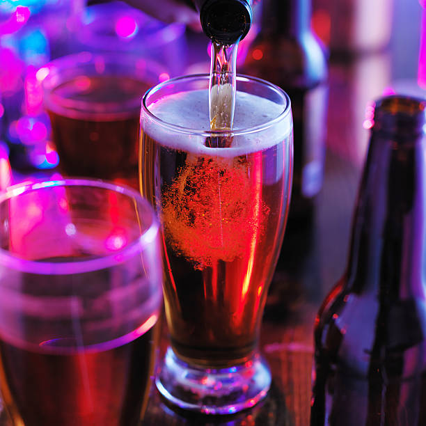 pouring beer into pint glass with colorful lighting at pub or bar