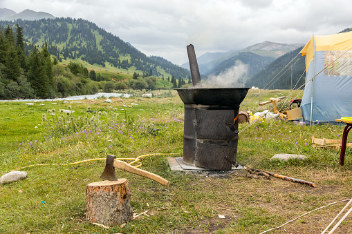 Vintage Style Traditional Iron Stove with Smoking Chimneys Green Meadow and Mountain Stream on Background