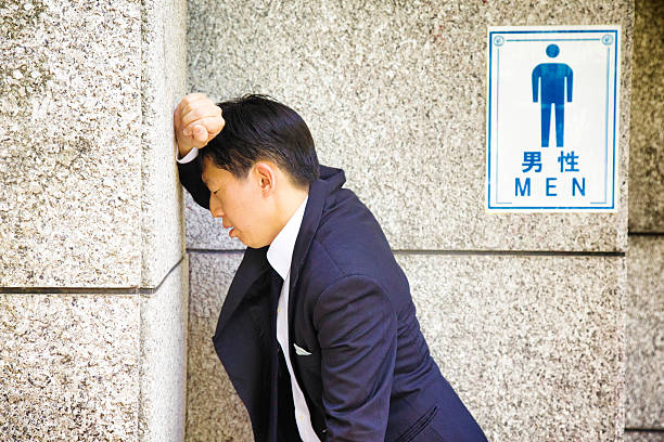 Suffering Japanese businessman rests against WC wall feeling sick Suffering Japanese businessman rests against public WC wall, feeling sick. toilet sign in japanese style stock pictures, royalty-free photos & images