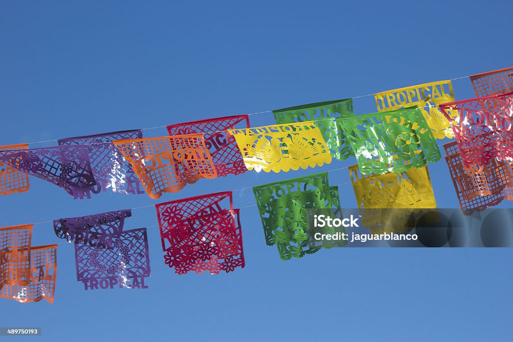 Mexican decorative Papers Mexican typical decorative papers called "Papel picado" with the word "Tropical" set over a street over a blue and clear sky. Papel Picado Stock Photo