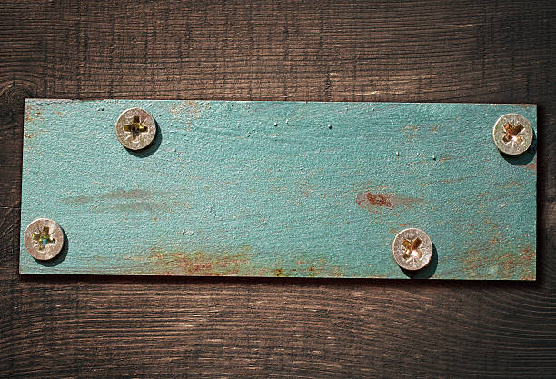 Metal plate screwed on dark brown wooden board.
