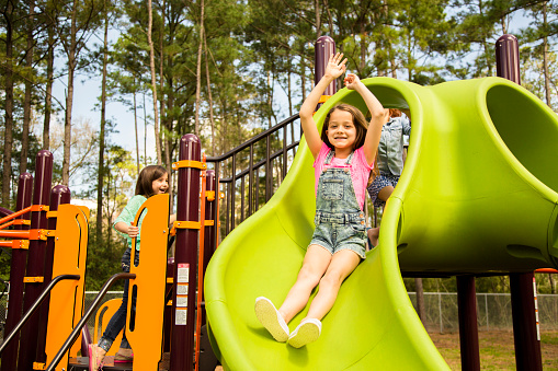 Three elementary age children play during school recess or at a park setting. Playground equipment, slide. 