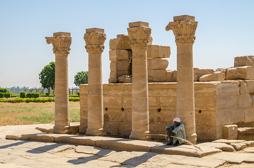 Luxor, Egypt, July 23 2014: There are columns near Dendera Temple in the picture. The Dendera Temple is a famous landmark of Egypt. There is an Arab sitting near the columns.