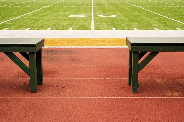 Two empty player benches at the 50 yard line of a college football field.