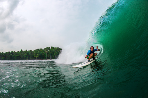A male surfer rides through a green indonesian tube.