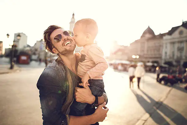 Photo of Loving little boy kissing his happy father in the city.
