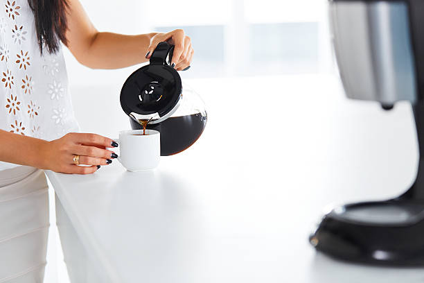 Woman's hand pouring coffee to a coffee cup Woman's hand with beautiful manicure pouring herself a mug of hot filtered coffee from a glass pot on her break. coffee maker in kitchen stock pictures, royalty-free photos & images