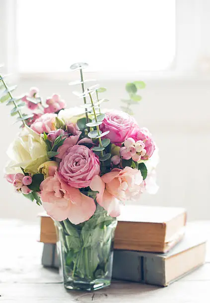 Elegant bouquet of pink flowers and ancient books on a tabke with backlight. Vintage decor.