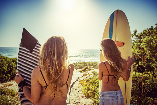 Surfer girls standing at the sea with surfboards, during a warm sunny summer day