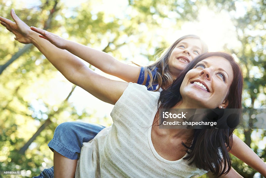 Soaring through the trees with mom Shot of smiling mother giving her cute daughter a piggyback while enjoying a sunny day outdoors Family Stock Photo