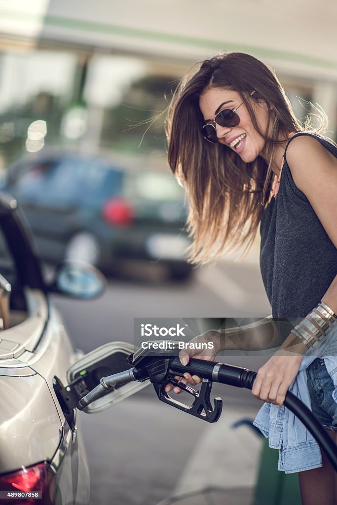 Smiling woman refueling her gas tank at fuel pump. Young happy woman pumping gas at gas station. Refueling Stock Photo