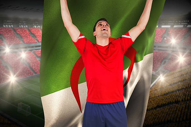 Excited football player cheering holding algeria flag Excited football player cheering holding algeria flag against vast football stadium with fans in yellow and red algeria soccer stock pictures, royalty-free photos & images