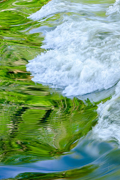 Spring leaves and blue sky are reflected in a flowing stream's cascade.