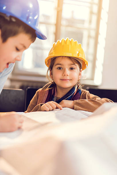 istock Smiling little girl architect studying blueprint and looking at camera. 489809410