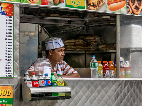 New York, USA - September 11, 2014: Hot dog vendor waits for customers at a New York kiosk.  