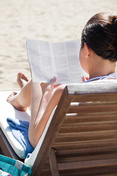 istock Woman reading book on deck chair at beach 489812562