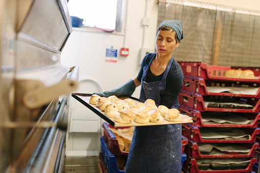 A baker removes scones from a commercial bread oven. Emma's Bread, Exeter, Devon. 