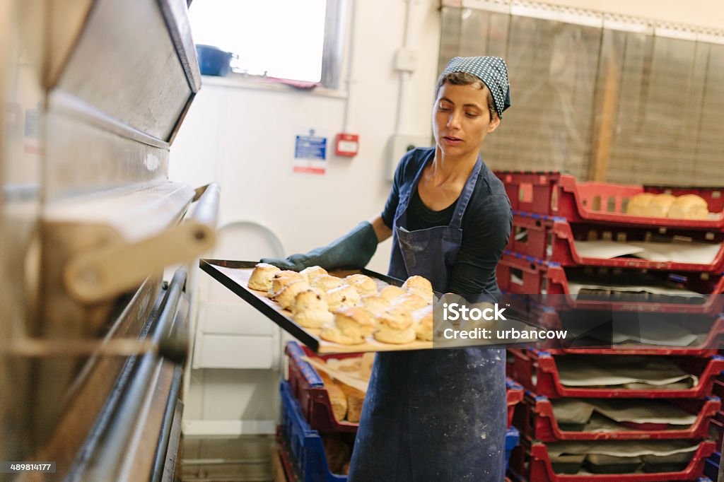 Freshly baked scones A baker removes scones from a commercial bread oven. Emma's Bread, Exeter, Devon.  Baker - Occupation Stock Photo
